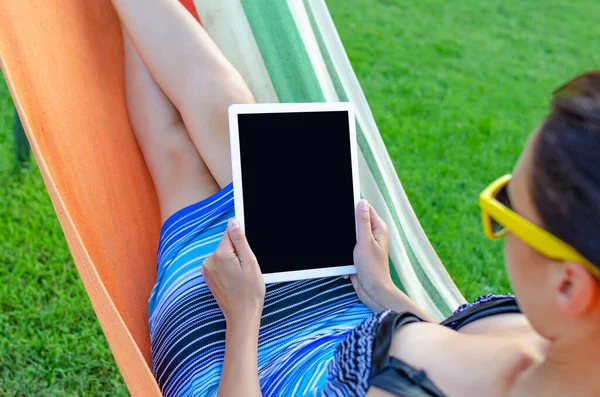 Mujer joven con una tableta en una hamaca . — Foto de Stock