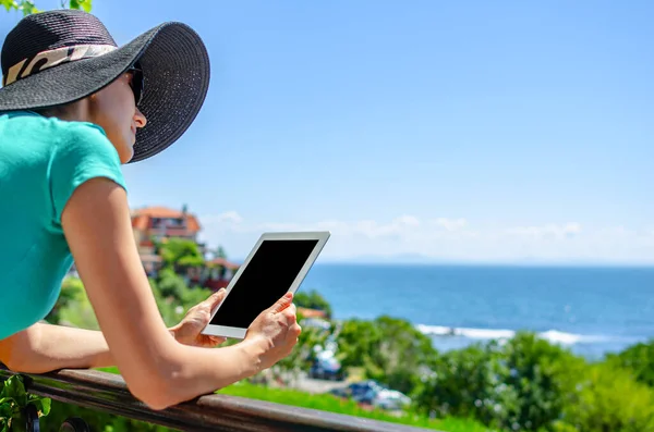 Jonge vrouw met een tablet in handen op een terras op de achtergrond van de zee. — Stockfoto