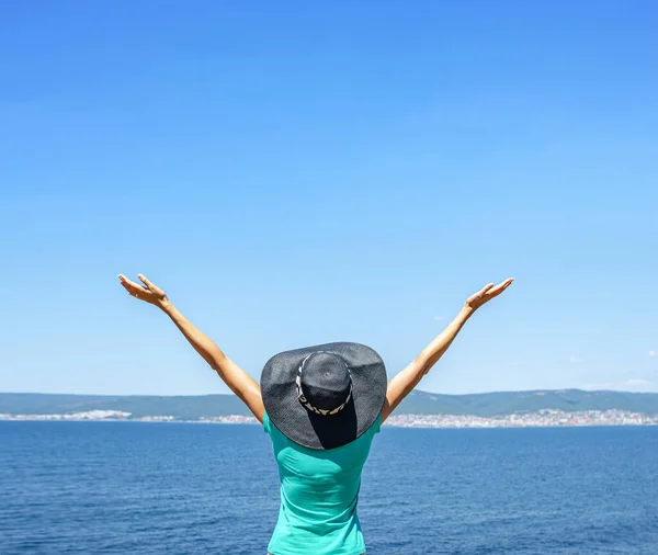 Young woman in a hat against the sea raises her hands up. — Stock Photo, Image