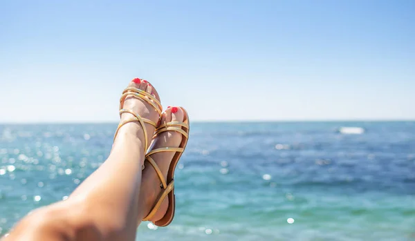 假期的概念。在阳光明媚的日子里，一双漂亮的女腿在大海的衬托下穿着凉鞋. — 图库照片