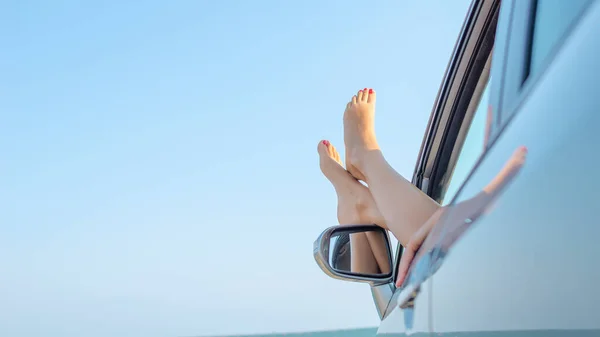 Weibliche Beine aus dem Autofenster vor dem Hintergrund einer Meereslandschaft. — Stockfoto