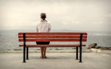 Yalnız kadın su kenarında bir bankta oturuyor. Tonu ayarlanmış resim.