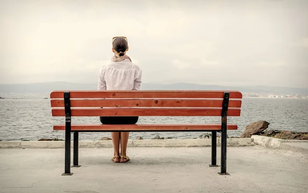 Donna sola siede su una panchina vicino all'acqua. Immagine tonica. — Foto Stock