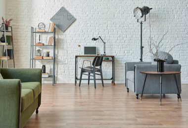 Modern beyaz tuğla duvar arka planı, yeşil ve gri kanepe, siyah mobilya detayı, kitaplık ile çalışma masası.