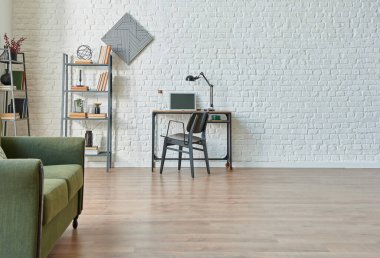 Modern beyaz tuğla duvar arka planı, yeşil ve gri kanepe, siyah mobilya detayı, kitaplık ile çalışma masası.