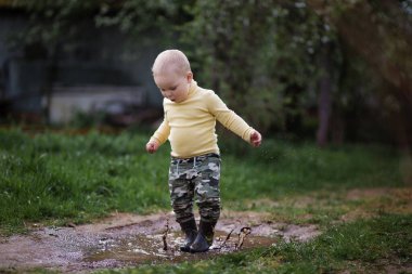 Su birikintisinde koşan lastik çizmeli küçük bir çocuk.