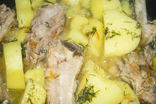 Stewed pork ribs with potatoes, onions, carrots and dill in a saucepan. Close up. Traditional recipe. Home cooking. — Stockfoto