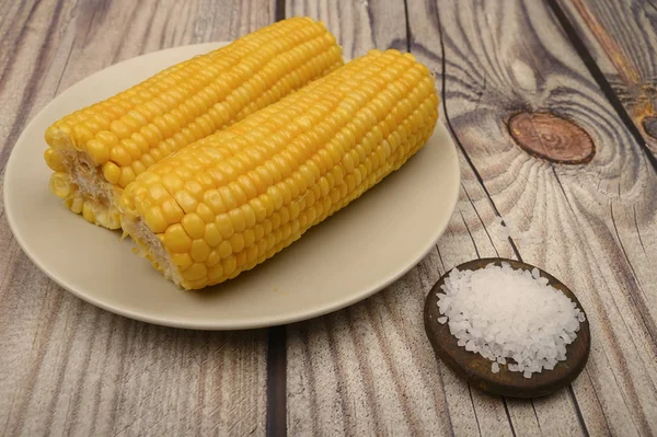 Due spighe di mais bollito in un piatto e sale grosso sul tavolo. Dieta sana. Dieta fitness. Per un dolce piacere . — Foto Stock