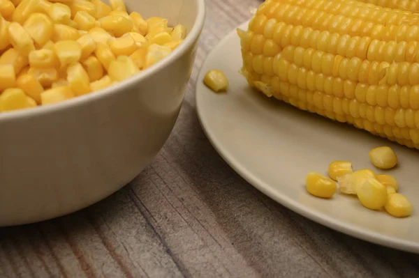 Два вуха вареної кукурудзи в тарілці і зерно кукурудзи на столі. Здорове харчування. Фітнес-дієта. Для солодкого частування. крупним планом . — стокове фото