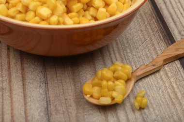 Tabaktaki mısır taneleri ve ahşap bir masadaki tahta kaşık. Fitness diyeti. Sağlıklı beslenme. Tatlı bir ikram için. Kapat..