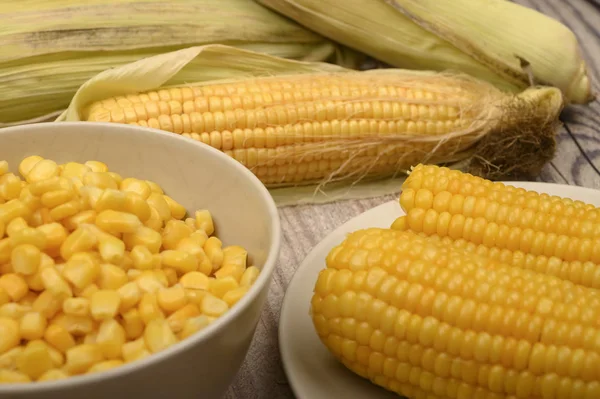 Two boiled ears of corn, corn kernels and untreated ears of corn on a wooden table. Fitness diet. Healthy diet. For a sweet treat. Close up.