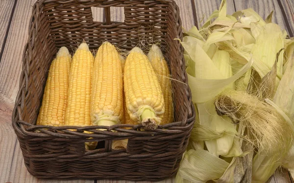 Очищенные колосья кукурузы в плетеной корзине и кукурузные листья на деревянном столе. Осенний урожай. Фитнес-диета. Здоровое питание. За сладкое угощение . — стоковое фото