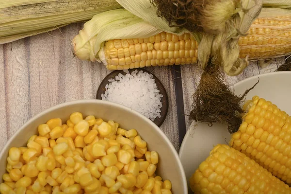 Two boiled ears of corn, corn kernels, coarse salt and raw ears of corn on a wooden table. Fitness diet. Healthy diet. For a sweet treat. Close up.