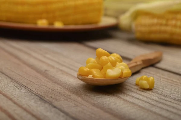 Grains of sweet corn on a wooden spoon on a wooden table, in the background boiled corn and untreated ears of corn. Fitness diet. Healthy diet. For a sweet treat. Close up. Selective focus.