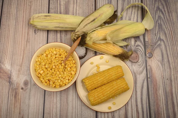 Grains of sweet corn in a plate with a wooden spoon, coarse salt and ears of corn on the table. Healthy diet. Fitness diet. For a sweet treat.