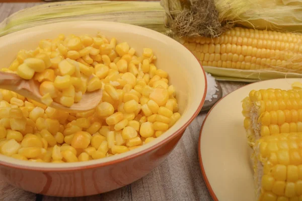 Grains of sweet corn in a plate and ears of corn on the wood table. Healthy diet. Fitness diet. For a sweet treat. Close up. — Stock Photo, Image