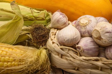 Kabuksuz bir mısır, hasır sepetinde taze sarımsak, mermer kabaklar ve masada sarı kabak. Sonbahar hasadı. Sağlıklı beslenme. Fitness diyeti. Tatlı bir ikram için. Kapat..