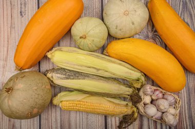 Kabuksuz bir mısır, hasır sepetinde taze sarımsak, mermer kabaklar ve masada sarı kabak. Sonbahar hasadı. Sağlıklı beslenme. Fitness diyeti. Tatlı bir ikram için.