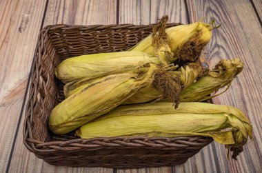 Tahta bir arka planda hasır sepette tedavi edilmemiş birkaç mısır. Sonbahar hasadı. Modern tarım. Sağlıklı beslenme. Tatlı bir ikram için. Kapat..