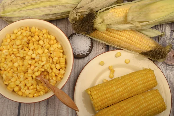 Granos de maíz dulce en un plato con una cuchara de madera, sal gruesa y espigas de maíz sobre la mesa. Dieta saludable. Dieta fitness. Para una golosina. De cerca. . —  Fotos de Stock