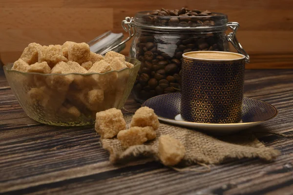 Eine Tasse Kaffee, Kaffeebohnen im Glas und braune Zuckerstücke auf einem hölzernen Hintergrund. — Stockfoto