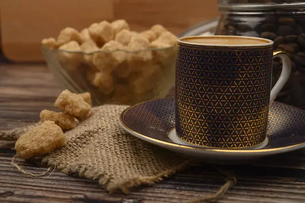 Чашка кави, шматочки коричневого цукру в цукровій мисці, кавові зерна в скляній банці на дерев'яному фоні . — стокове фото