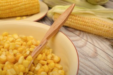 Tahta kaşıkla tabakta mısır taneleri ve masada mısır taneleri. Sağlıklı beslenme. Fitness diyeti. Tatlı bir ikram için. Kapat..