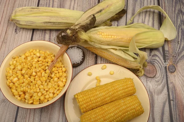 Зерна сладкой кукурузы в тарелке с деревянной ложкой, грубой солью и колосьями кукурузы на столе. Здоровое питание. Фитнес-диета. За сладкое угощение . — стоковое фото