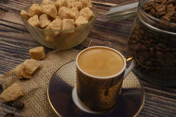 Eine Tasse Kaffee, braune Zuckerstücke in einer Zuckerdose, Kaffeebohnen in einem Glas auf einem hölzernen Hintergrund. — Stockfoto