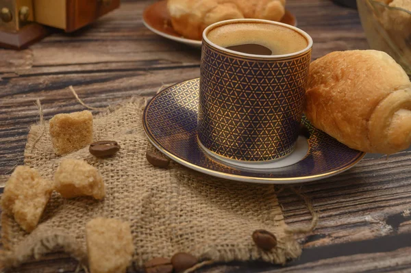 Eine Tasse Kaffee, braune Zuckerstücke und ein Croissant auf einem hölzernen Hintergrund. — Stockfoto