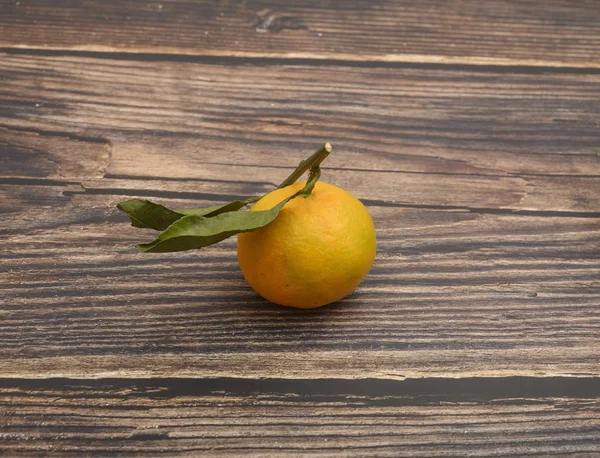 Dal üzerinde sarı bir mandalina ve ahşap bir arka planda yeşil yapraklar. Sonbahar hasadı. Modern tarım. Tatlı bir ikram için. — Stok fotoğraf