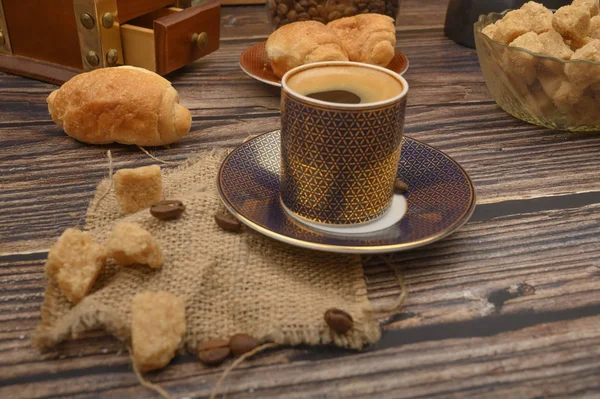 Eine Tasse Kaffee, braune Zuckerstücke in einer Zuckerdose und Croissants auf einem hölzernen Hintergrund. — Stockfoto