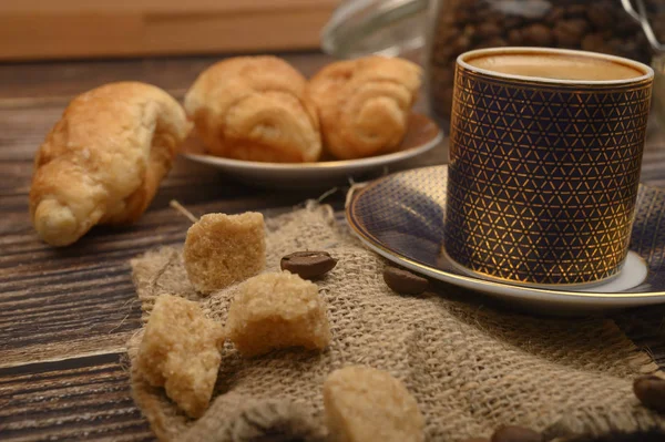 Eine Tasse Kaffee, brauner Zucker, Croissants auf einem hölzernen Hintergrund. Nahaufnahme. — Stockfoto