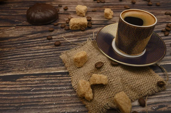 Eine Tasse Kaffee, braune Zuckerstücke, Marshmallows in Schokolade und Kaffeebohnen auf einem hölzernen Hintergrund. Nahaufnahme. — Stockfoto