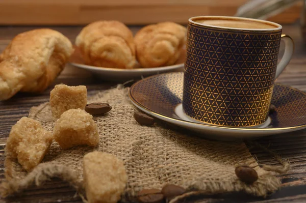 Kaffeetasse, brauner Zucker, Croissants, Kaffeebohnen auf Holzgrund. Nahaufnahme. — Stockfoto