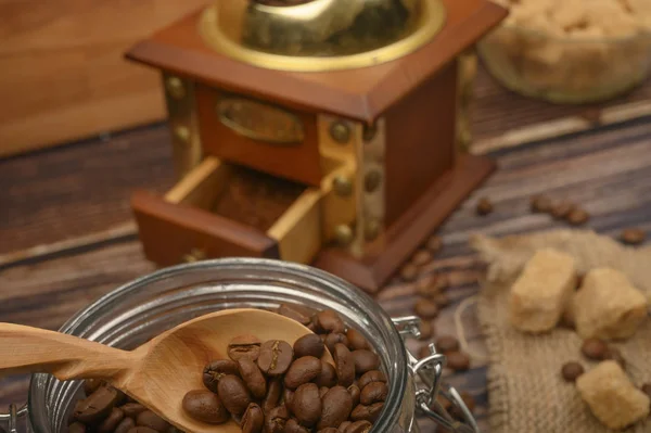 Wooden spoon in a glass jar with coffee beans, coffee grinder, pieces of brown sugar on a wooden background. Close up. Stock Image