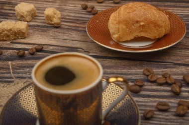 Kahve fincanı, kruvasan, esmer şeker ve ahşap arka planda kahve çekirdeği. Kapat..