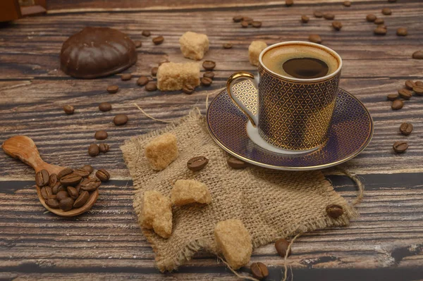 Cup of coffee, brown sugar, coffee beans, marshmallows in chocolate on wooden background.