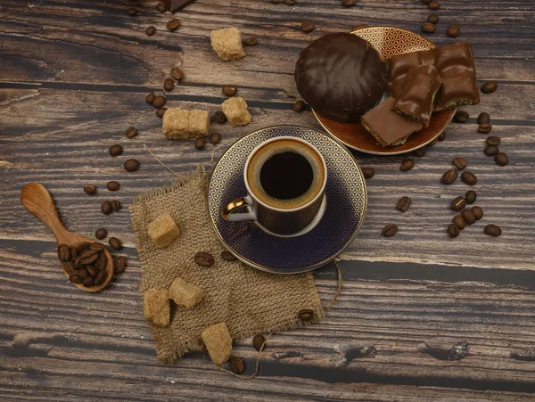 Eine Tasse Kaffee, Kaffeebohnen, brauner Zucker, Schokoladenstücke, Marshmallows in Schokolade auf Holzgrund. — Stockfoto