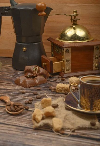 Coffee Cup, coffee beans, brown sugar, chocolate pieces, coffee maker, coffee grinder on wooden background.