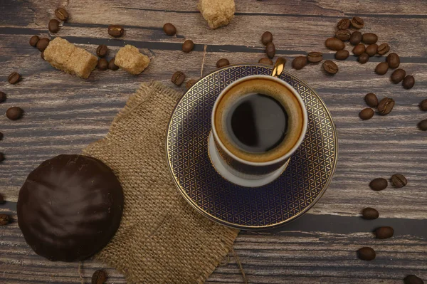 Eine Tasse Kaffee, Marshmallows in Schokolade, Kaffeebohnen, brauner Zucker auf einem Holzuntergrund. Nahaufnahme. — Stockfoto