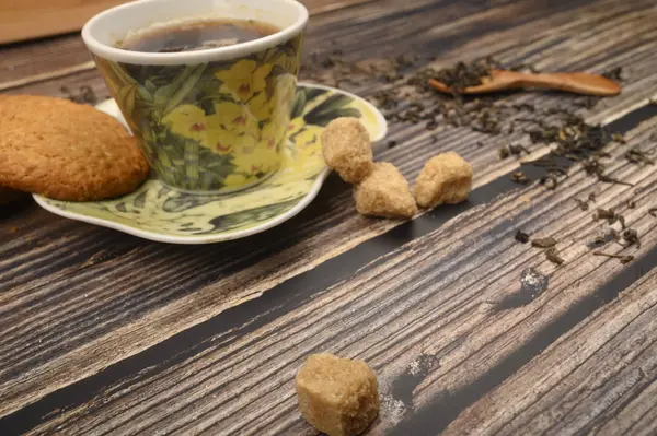 Eine Tasse schwarzen Tee, Teeblätter, braunen Zucker, Haferflockenkekse auf einem hölzernen Hintergrund. Nahaufnahme. — Stockfoto
