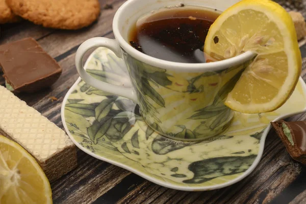 Eine Tasse schwarzen Tee, Zitronenscheiben, braune Zuckerscheiben, Haferflockenkekse, Waffeln auf einem hölzernen Hintergrund. Nahaufnahme. — Stockfoto