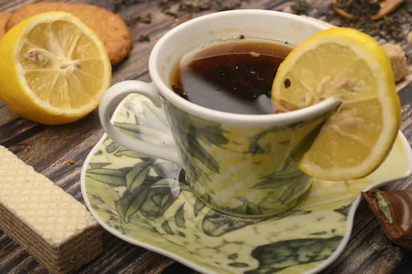 A Cup of black tea, sliced lemon, brown sugar slices, oatmeal cookies, waffles on a wooden background. Close up. — Stock Photo, Image