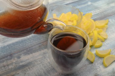 Siyah çay çaydanlıktan bardağa dökülür, marmelat limon dilimleri de ahşap zemine. Kapat..