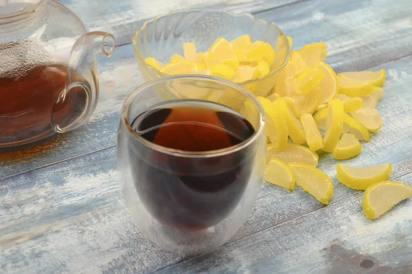 Лимонные ломтики мармелада, стакан черного чая и чайник с вареным чаем на деревянном фоне. Милый десерт. Закрыть . — стоковое фото