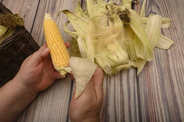 Руки человека чистят ухо от кукурузы на деревянном фоне. Осенний урожай, здоровая пища, фитнес-диета. Закрыть . — стоковое фото