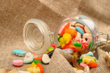 Kaba ev yapımı kumaşın arka planında cam bir kavanozda çok renkli marmelat. Lezzetli tatil hediyesi..