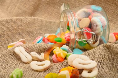 Kaba ev yapımı kumaşın arka planında cam bir kavanozda çok renkli marmelat. Lezzetli tatil hediyesi..