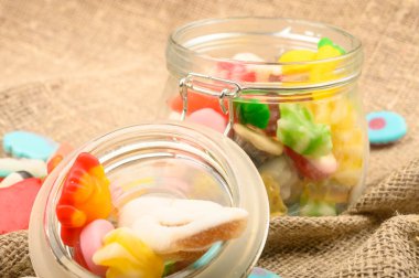 Kaba ev yapımı kumaşın arka planında cam bir kavanozda çok renkli marmelat. Lezzetli tatil hediyesi..